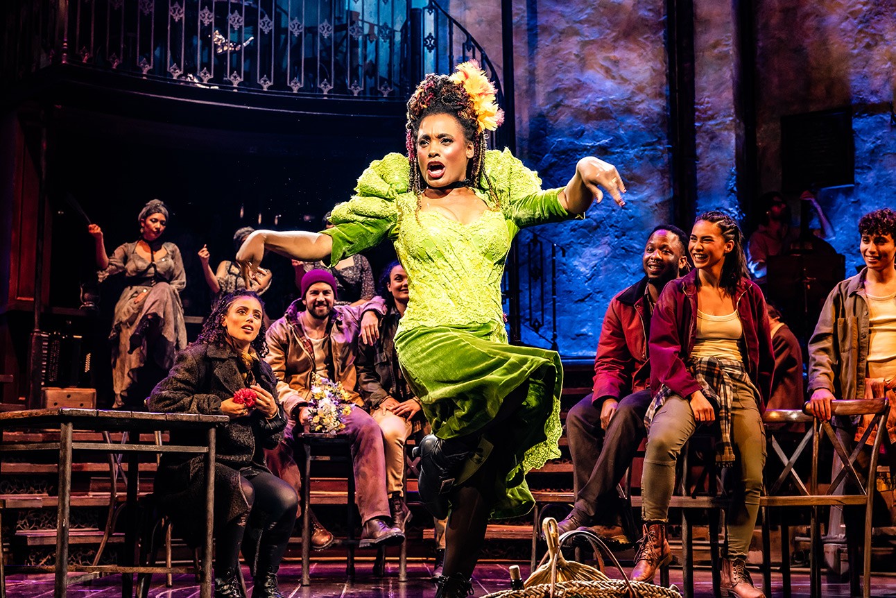 Joy Wielkens as Persephone sings passionately in a dimly lit, rustic Hadestown stage setting.