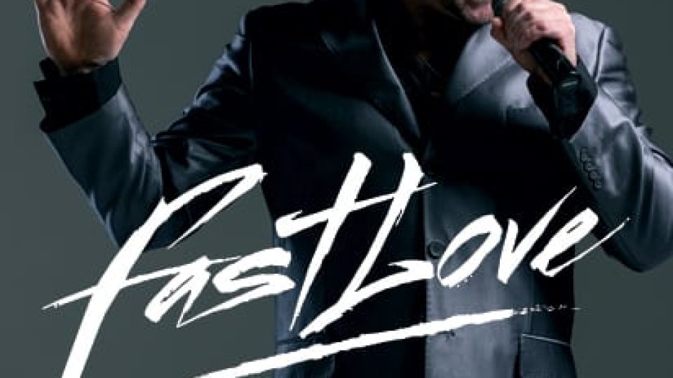 A man in a silver suit sings joyfully, with dramatic stage lighting behind him.