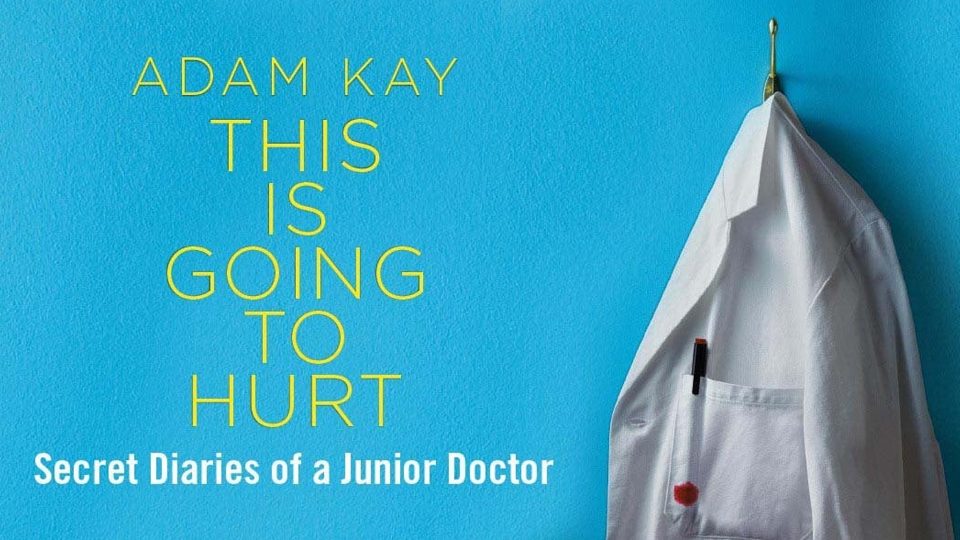 A white lab coat hangs on a hook against a bright blue wall.