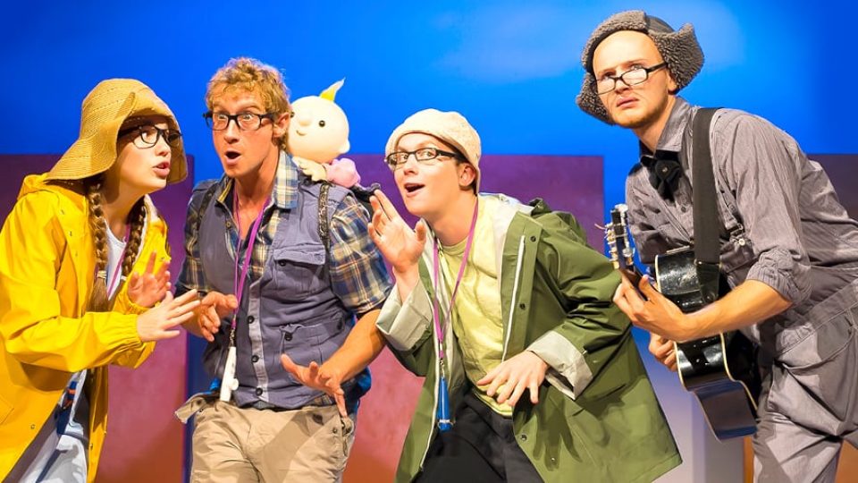 Four actors in colourful costumes, expressing excitement in a playful theatrical setting.