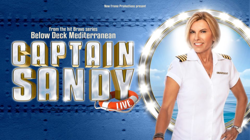 A woman in a white captain's uniform smiles against a blue ocean background.