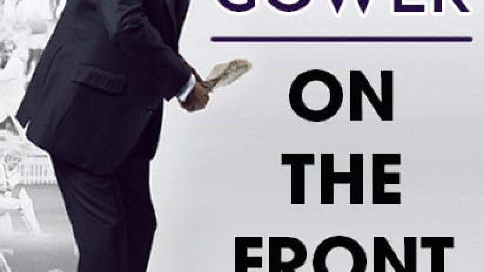 David Gower poses in a dark suit, holding a cricket bat with a faded sports backdrop.