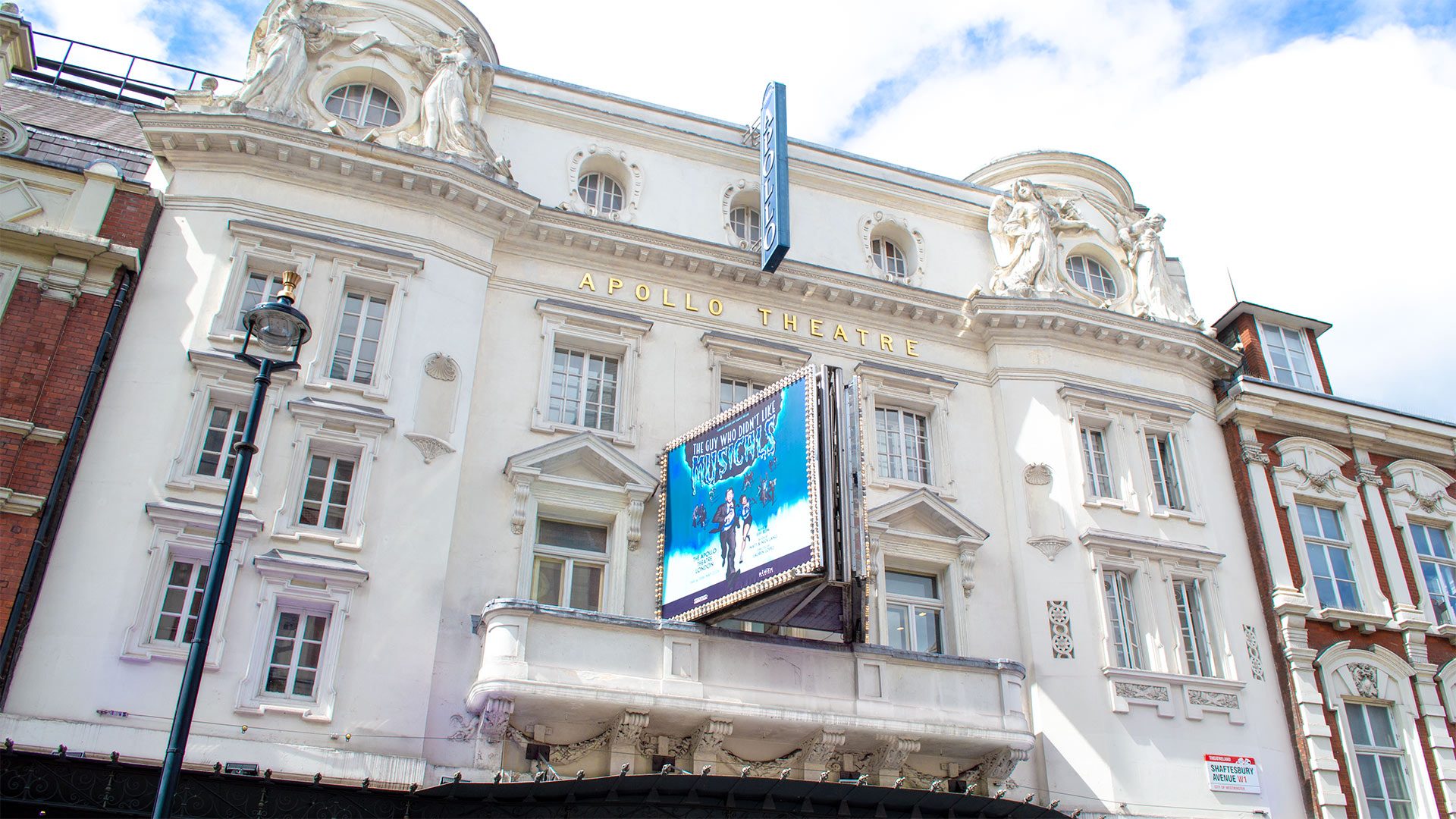 Apollo Theatre facade with ornate architecture, large blue and white show poster, and clear sky above.