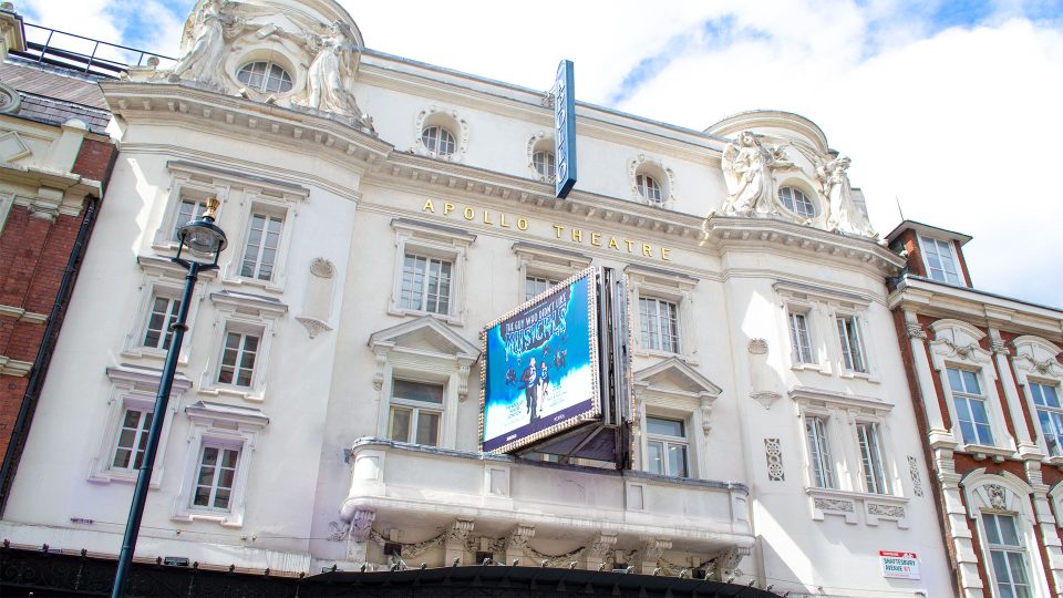 Apollo Theatre facade with ornate architecture, large blue and white show poster, and clear sky above.