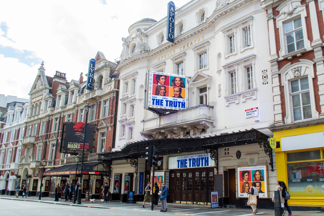 Apollo Theatre exterior with "The Truth" posters, white façade, and people walking on the street.