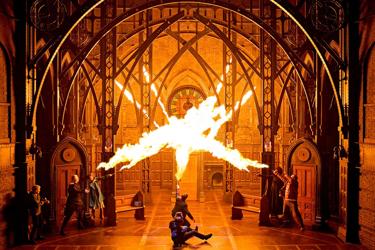 Stage scene from "Harry Potter and the Cursed Child" with dramatic fire effect and gothic arches.