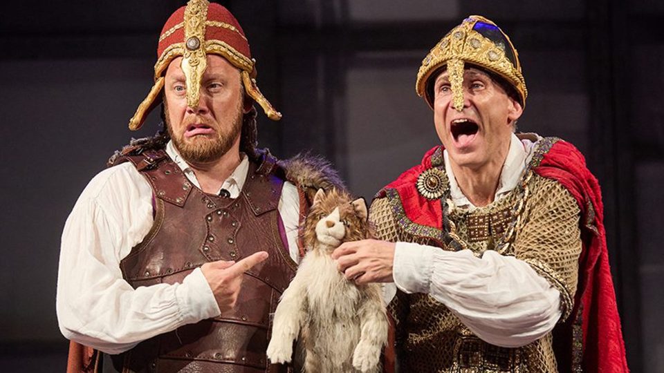 Two actors in historical costumes, one holding a puppet, with dramatic expressions.