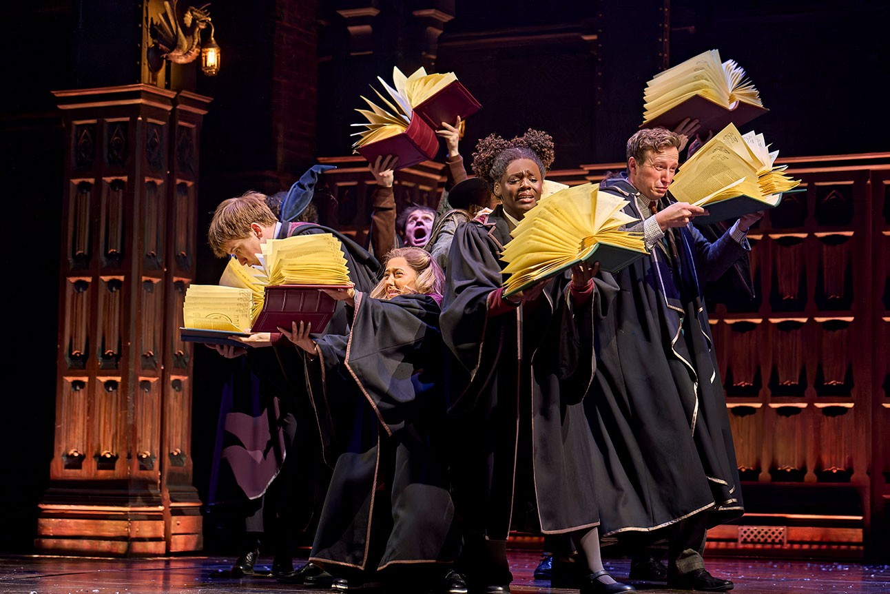 Actors in robes energetically holding large, open books on stage during "Harry Potter and the Cursed Child".