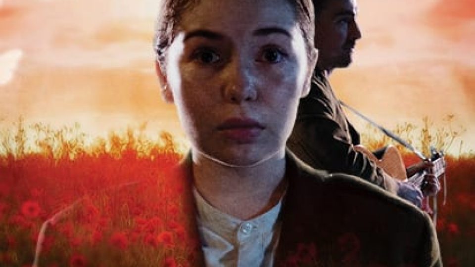 A woman in a dark jacket and a man with a guitar against a sunset background.