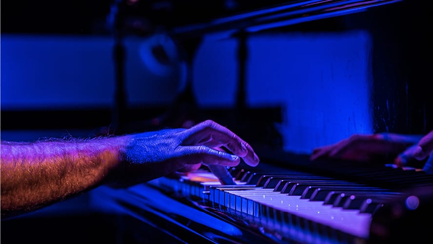 A close-up of a man's hand playing piano keys, with blue lighting reflections.