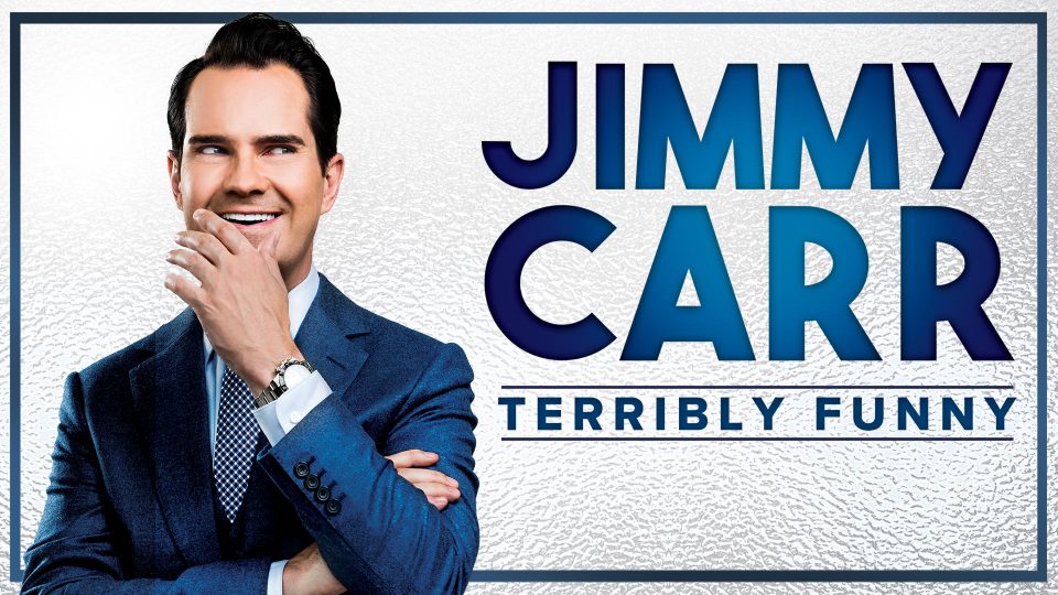 A smiling man in a blue suit poses with his hand on his chin.