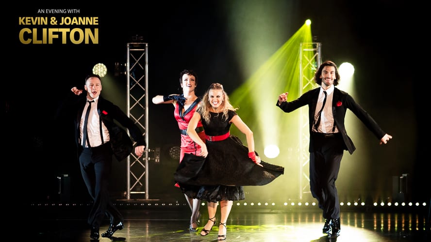 Three dancers in formal attire energetically perform under vibrant stage lighting.