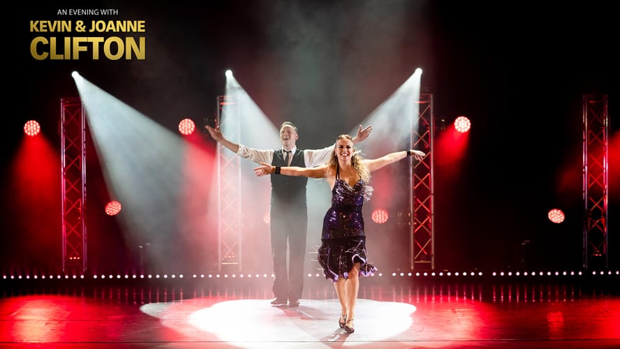 Kevin and Joanne Clifton perform on stage, illuminated by dramatic lighting and vibrant costumes.