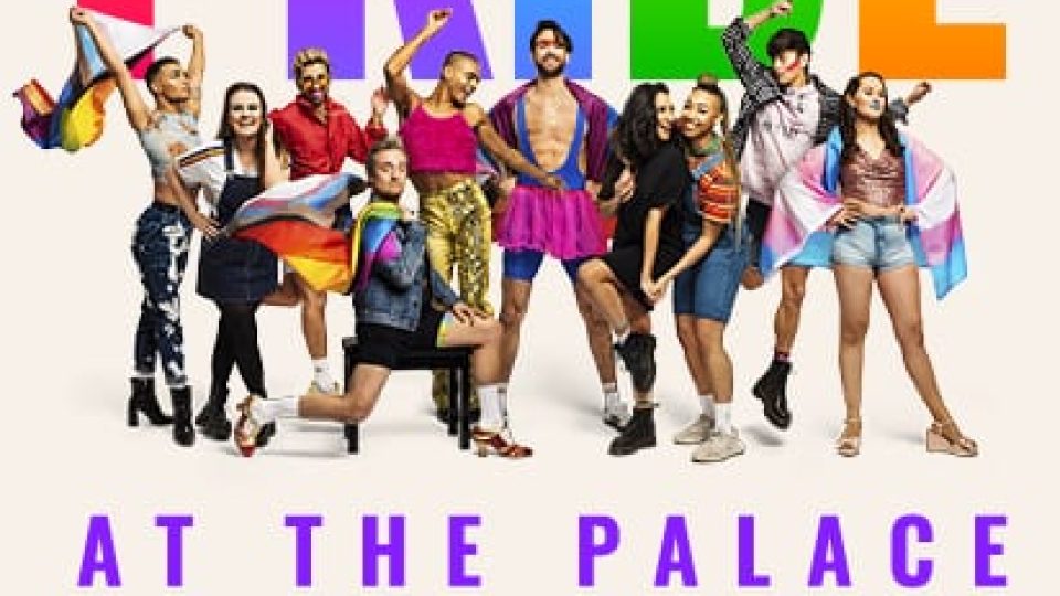 A diverse group of performers in vibrant outfits celebrates Pride against a light backdrop.