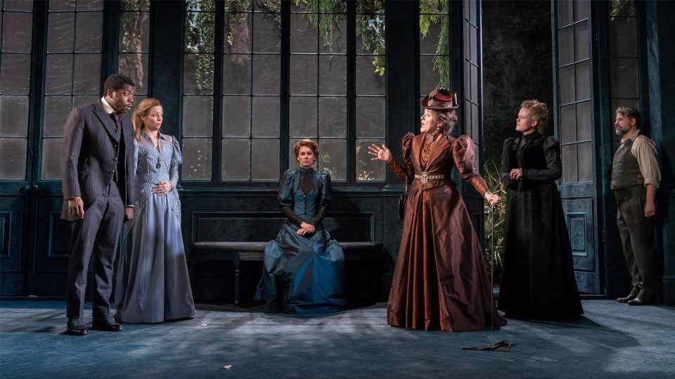 A scene from 'The Importance of Being Earnest' featuring five actors in period costumes.