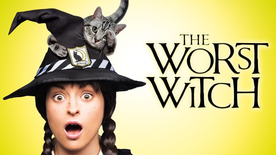 A surprised girl with braids wears a black witch hat and a grey cat.