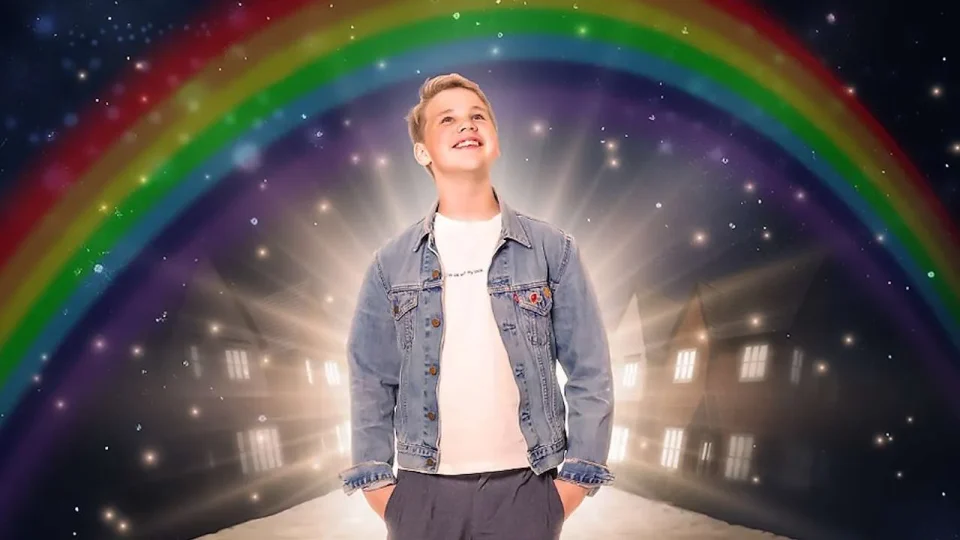 A boy smiling under a rainbow, with a glowing background and houses visible.