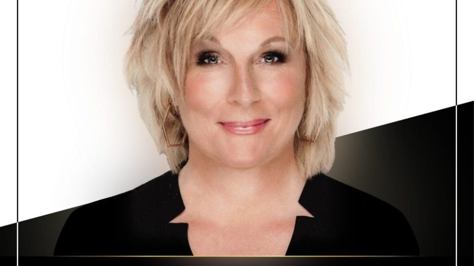 A smiling woman with blonde hair appears on a promotional poster with a black background.