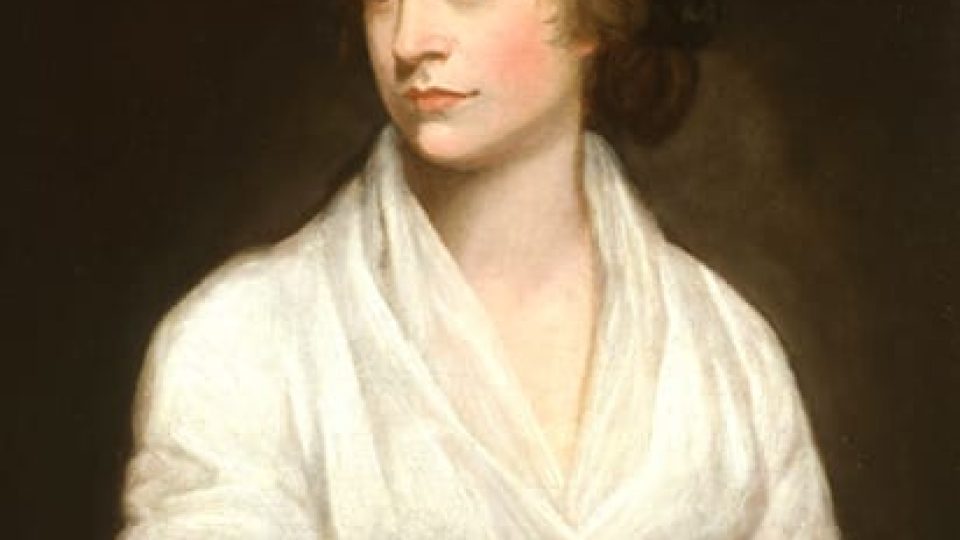 Portrait of a woman with light skin and brown hair, dressed in white against a dark backdrop.