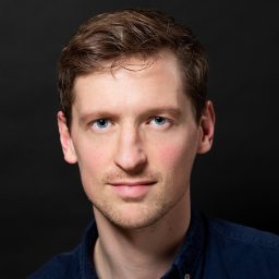 Liam Wrate in character costume, smiling, against a plain dark background for The Producers.