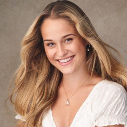 Smiling woman with long blonde hair wearing a white top, neutral background.