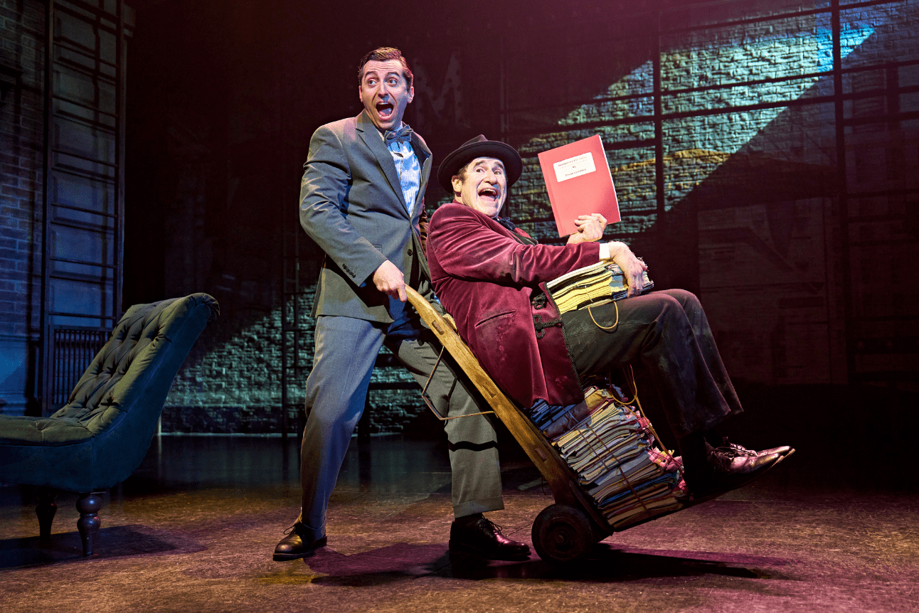 Marc Antolin wheels off Richard Kind who is sat on a trolley piled high with scripts