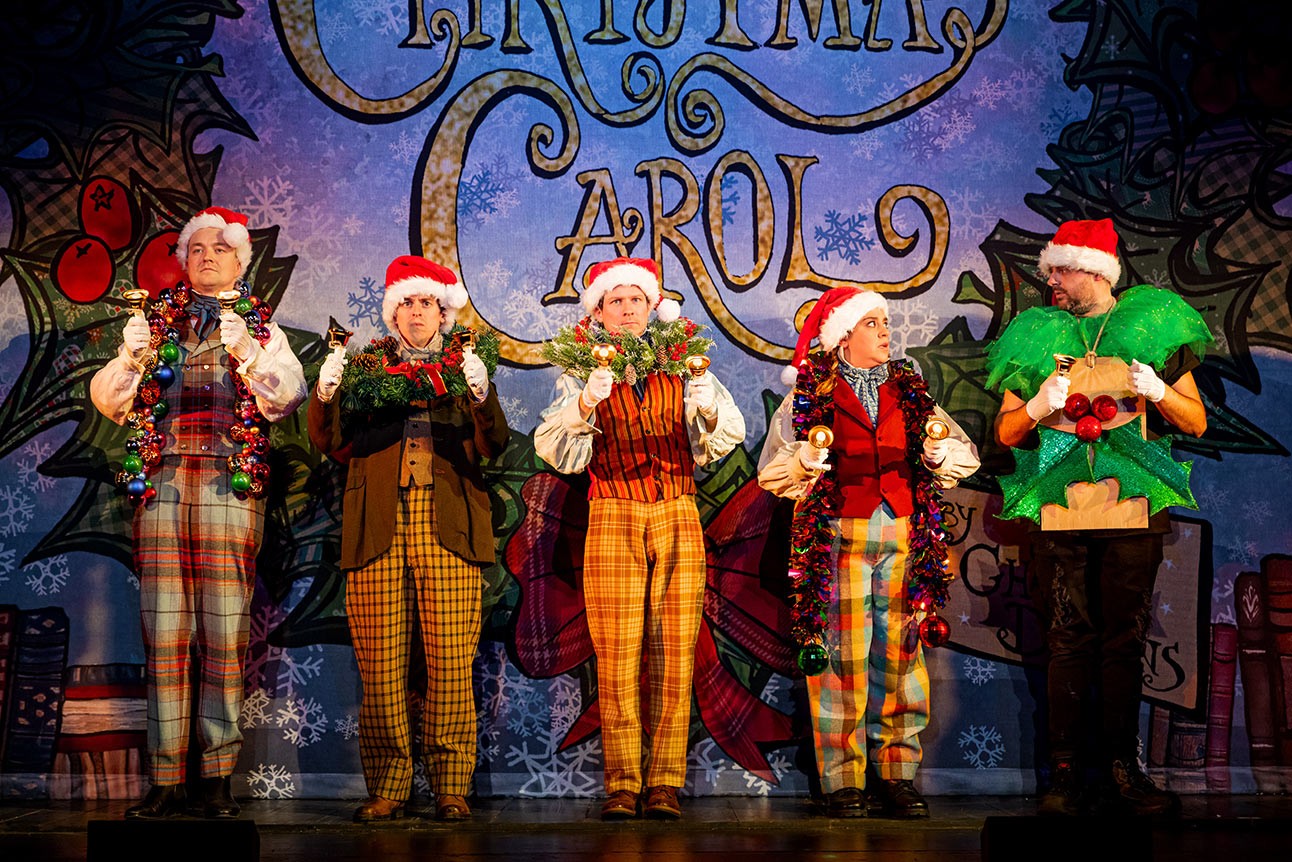 Cast of Christmas Carol Goes Wrong in festive costumes, posing together against a plain white background.