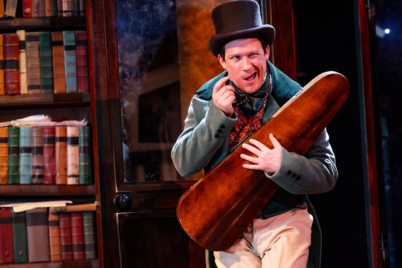 Matt Cavendish in festive costume, holding a script, with a decorated Christmas tree in the background.