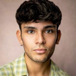 A young man with short dark hair and a green checked shirt against a neutral background.