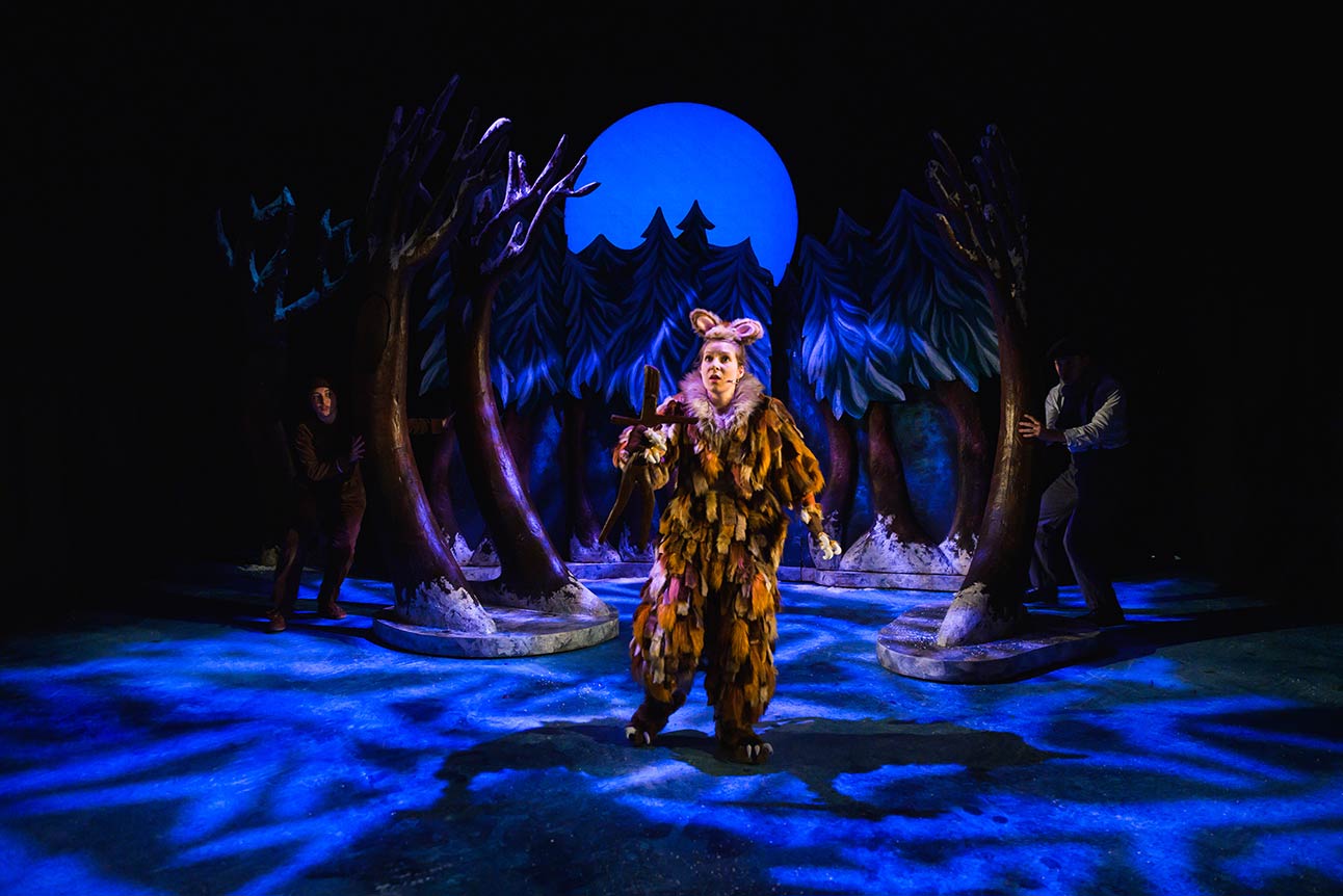 The Gruffalo's Child stands in a snowy forest, illuminated by blue and purple stage lighting.