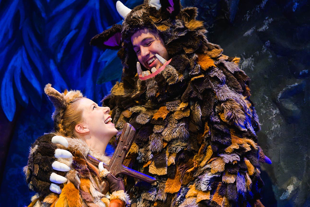 A joyful woman and a large, furry creature share a moment against a vibrant blue background.