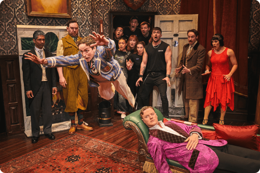 Actors in costume perform a comedic scene in a richly decorated interior.