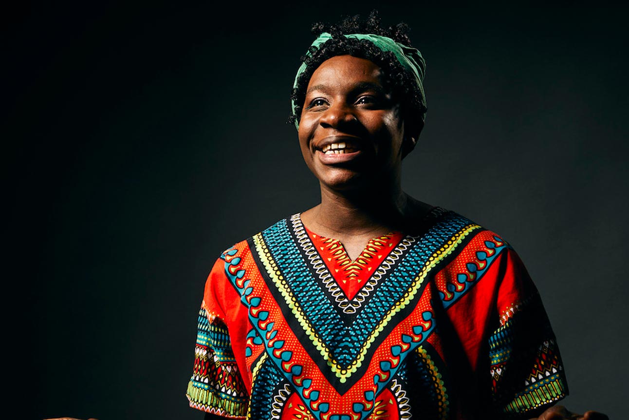 A joyful person wearing a colourful shirt, gesturing with hands against a grey backdrop.
