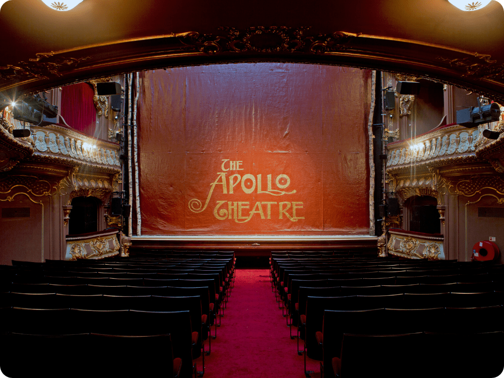 Interior of Apollo Theatre featuring red curtains, ornate gold detailing, and empty black seating.