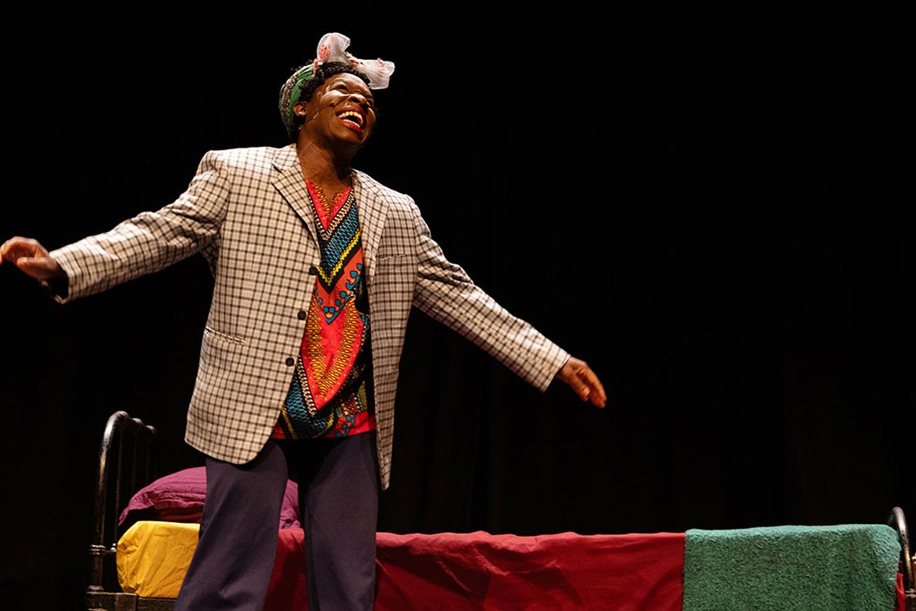 A person in a checked blazer and colourful shirt, joyfully performing on stage.