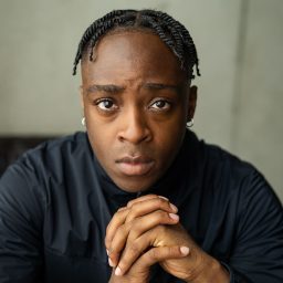 Alex Okoampa, wearing a blue shirt, against a plain light grey background.