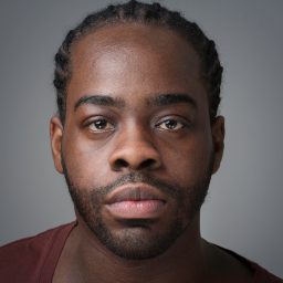 Daniel Haswell in a dark shirt, smiling against a plain grey background.