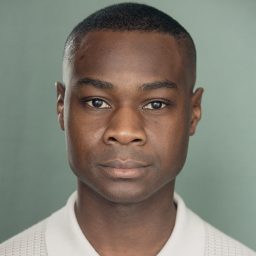 Eddie Elliott wearing a dark shirt, smiling against a plain grey background in a professional headshot.