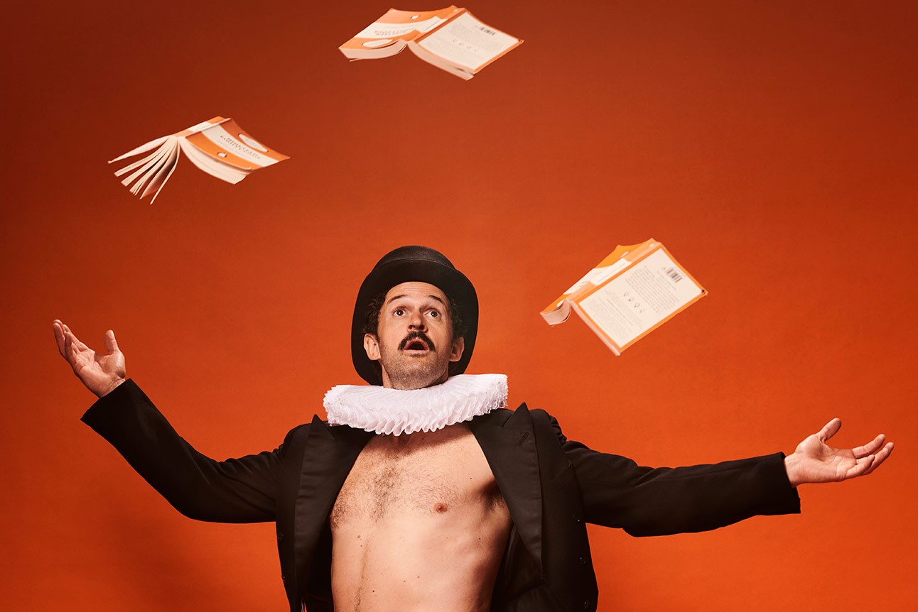 Garry Starr wearing a black hat, ruff collar, and open jacket, tossing white papers against an orange background.