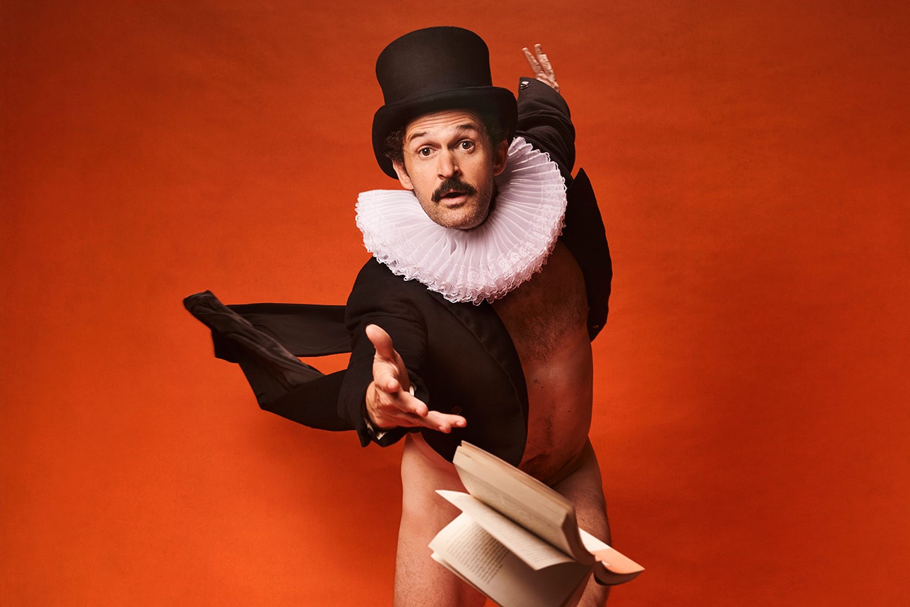 Garry Starr in Renaissance costume with ruff collar and top hat, gesturing expressively against orange backdrop.