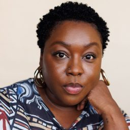 Helena Pipe smiling, wearing a dark top, with a blurred neutral background behind her.