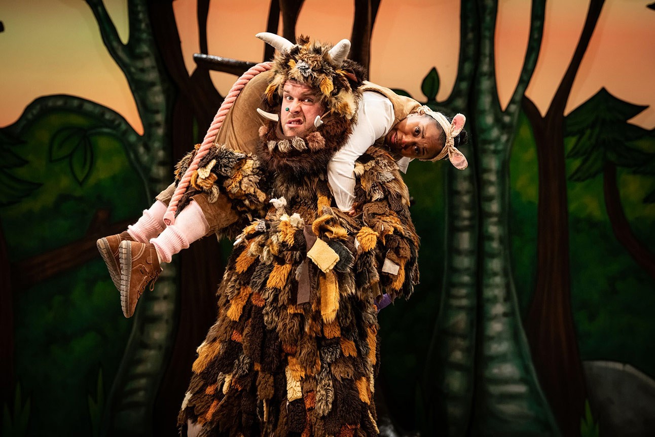 A performer in a Gruffalo costume carries another in a pink mouse outfit on stage.