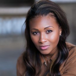 Lori Barker smiling, wearing a black top, with a blurred neutral grey background.