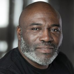 Mccallam-Connell smiles wearing a dark blazer against a plain grey background in a professional headshot.