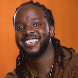 Tad Hapugati smiles in a blue shirt against a plain grey background in this headshot.