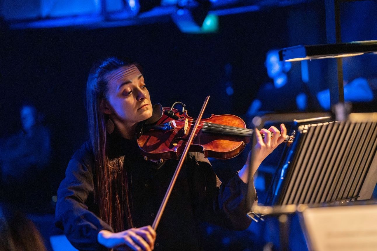 A woman plays the violin under blue stage lighting.