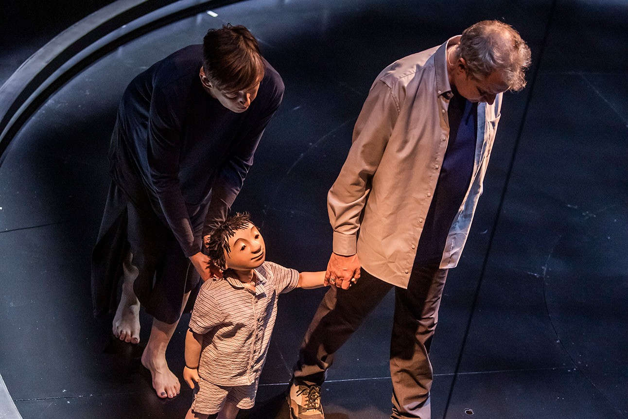 Phelim McDermott and Sarah Wright with puppet on stage, holding hands, dimly lit setting.