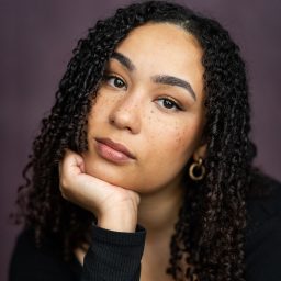 Eliza Waters with shoulder-length brown hair, smiling against a plain light grey background.