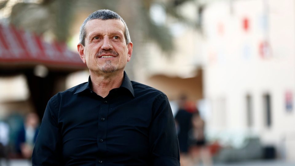 Guenther Steiner in a black shirt, looking slightly right, with a blurred outdoor background.