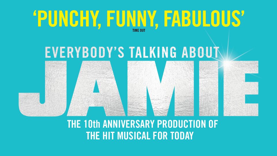 Jamie, wearing a red jacket and glasses, stands smiling against a colourful urban mural background.